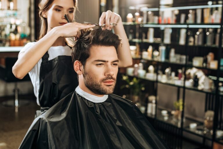 stylist cutting a man's hair with scissors and a comb at the salon